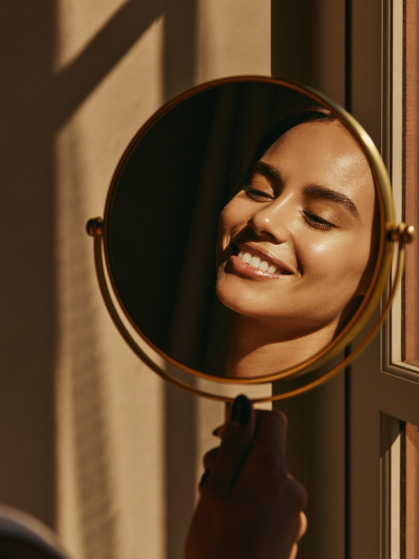 Client smiling at her restored brows in a brass hand mirror at Aileen's Beauty, Campbell CA